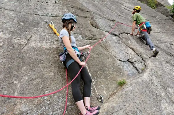 female climber belaying on rock while partner climbs